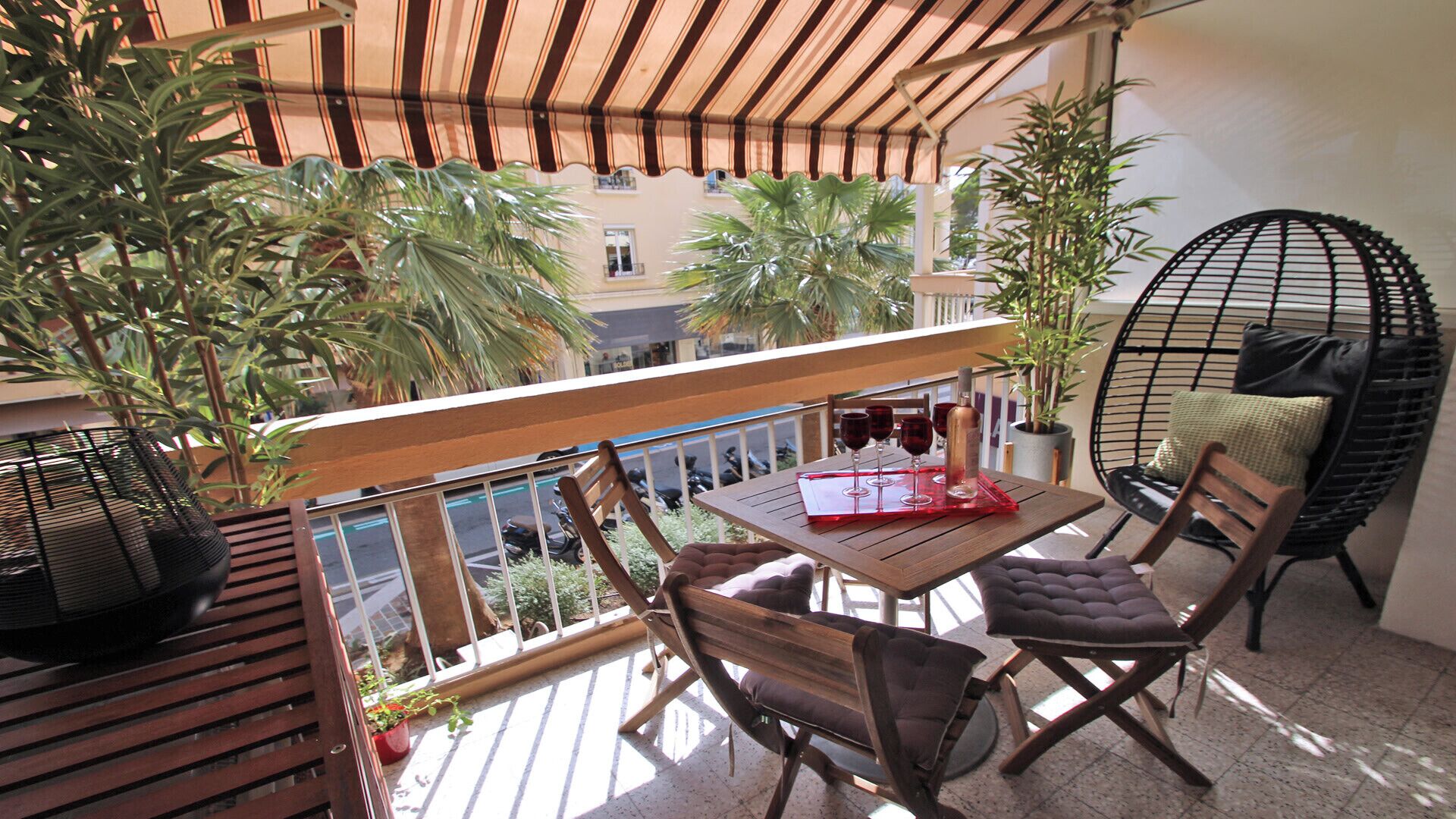 A balcony with wooden furniture, a table with wine glasses, and potted plants.