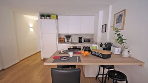 Una cocina compacta con armarios blancos, encimera de madera, cafetera, microondas y una pequeña planta en maceta.