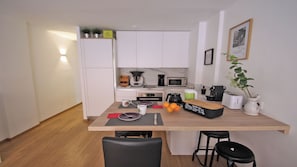 Una cocina compacta con armarios blancos, encimera de madera, cafetera, microondas y una pequeña planta en maceta.