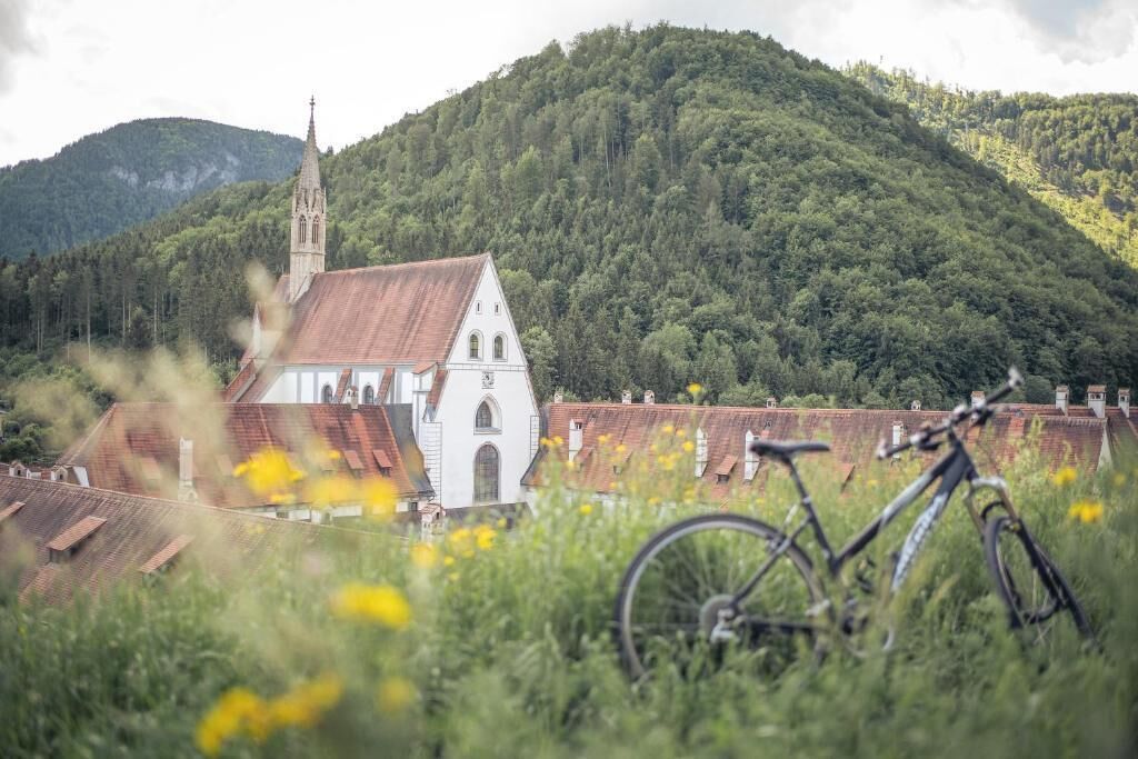 Uma igreja com um campanário, rodeada por vegetação exuberante e uma bicicleta em primeiro plano.