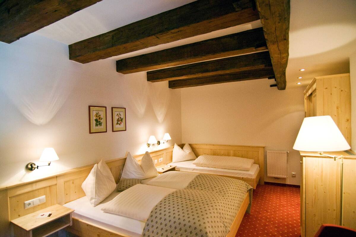 A hotel room with two beds, wooden beams, a radiator, and wall-mounted lamps.