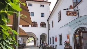 A courtyard with cobblestone flooring, a white building with a sign reading "Kartausekeller," and a red-roofed tower in the background. - Hotel Kartause (Gaming)