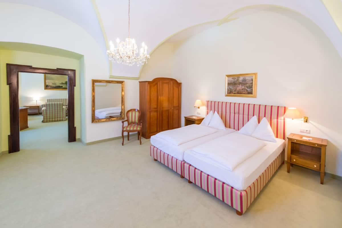A bedroom with a large bed, a wooden wardrobe, a chair, a mirror, and a chandelier.
