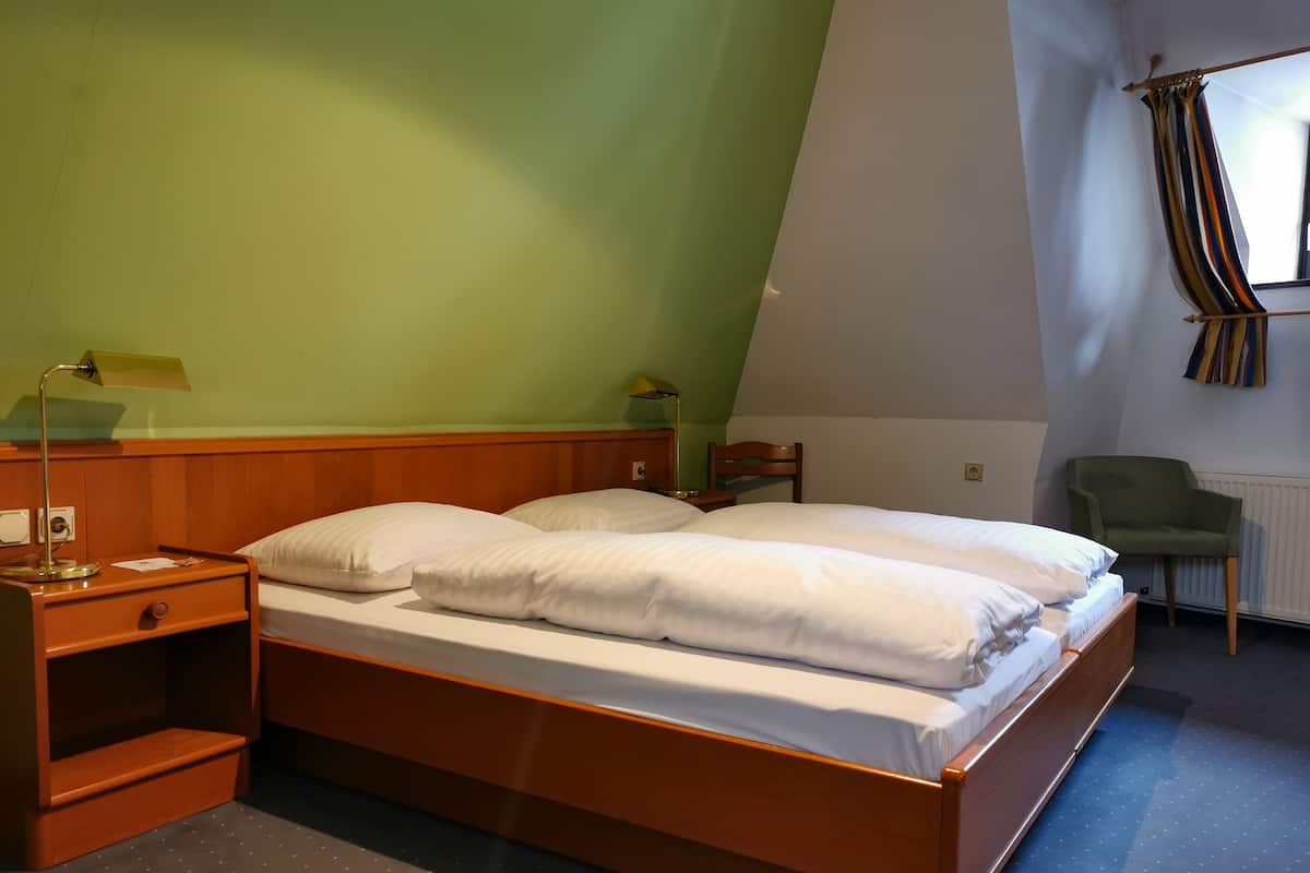 A bedroom with a wooden bed, a nightstand, a lamp, a chair, and a window with curtains.