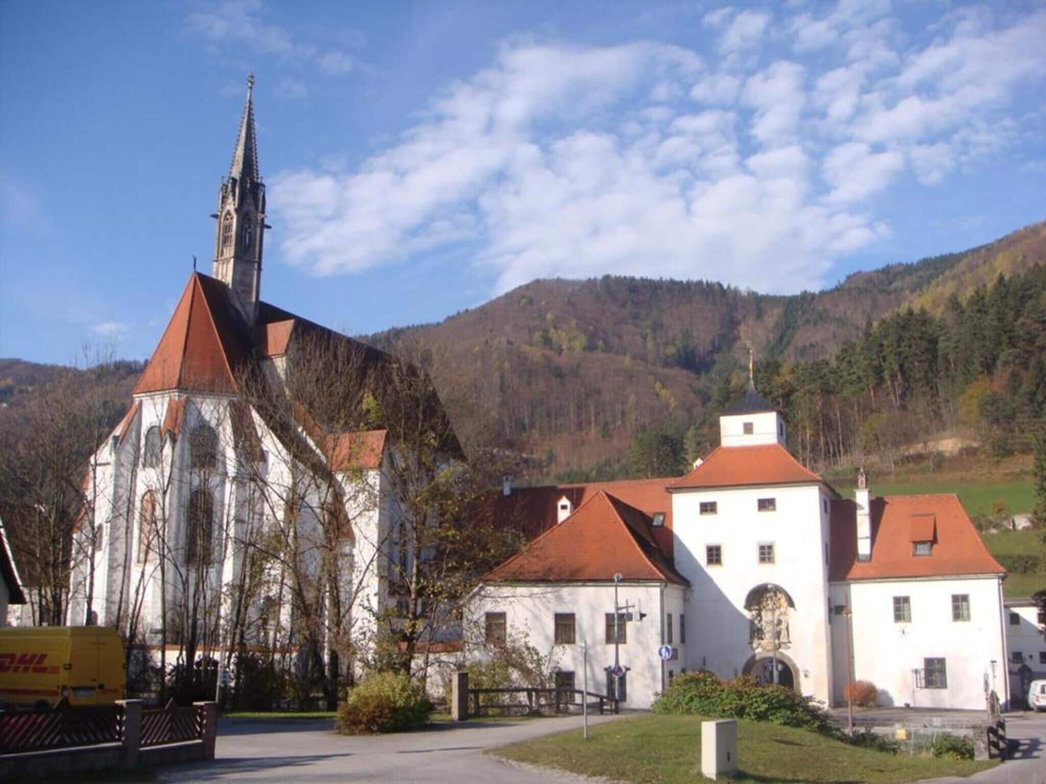 Eine Kirche mit einem hohen Kirchturm und ein kleineres Gebäude mit rotem Dach im Vordergrund.