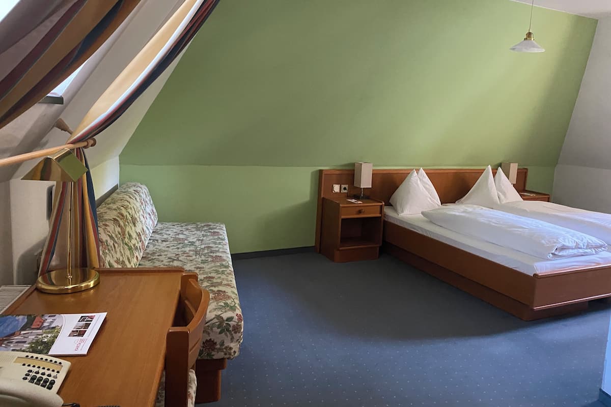 A hotel room with a bed, a desk with a telephone, a nightstand, and a lamp.