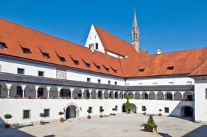A courtyard with white buildings, red roofs, and a church spire in the background. - Hotel Kartause (Gaming)