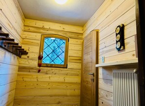 Ein Holzblockhaus-Innenraum mit Fenster, Heizkörper und einem an der Wand befestigten Thermometer.