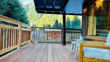 A wooden deck with a bed and a table, overlooking a forested mountain.