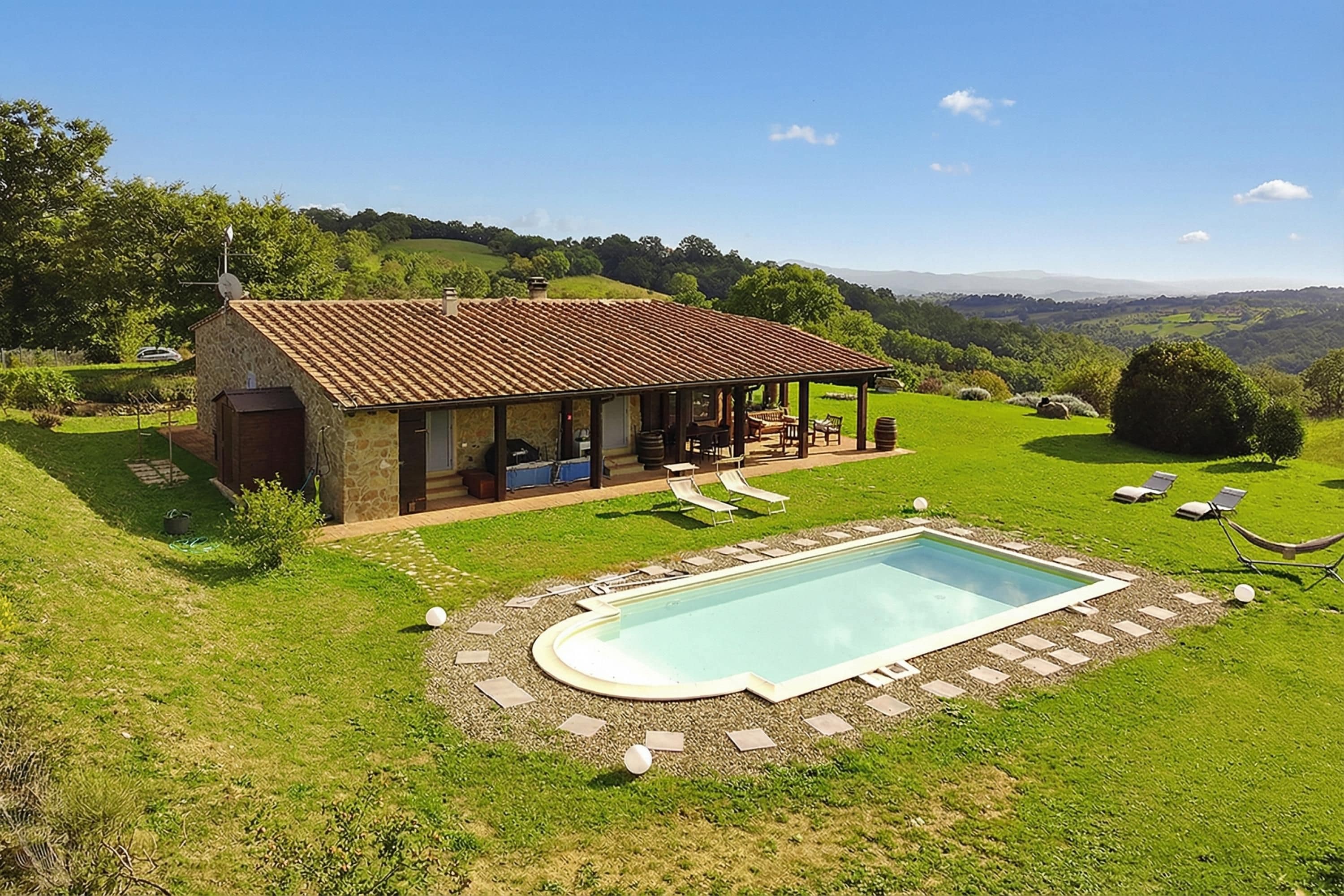 A stone house with a pool, outdoor seating, and a view of rolling hills.