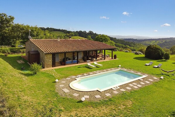 A stone house with a pool, outdoor seating, and a view of rolling hills.