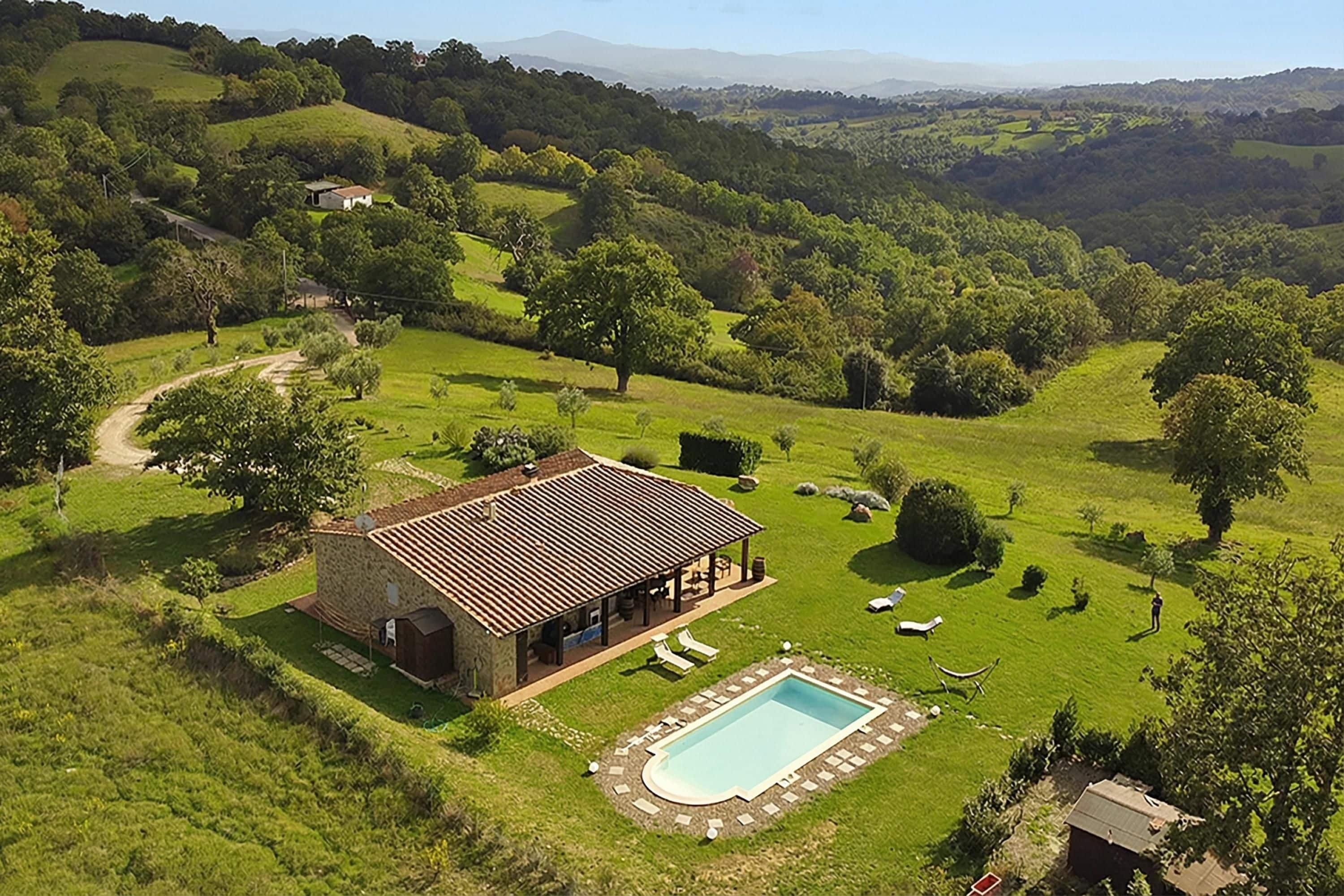 A house with a pool, surrounded by a lush green landscape and hills.