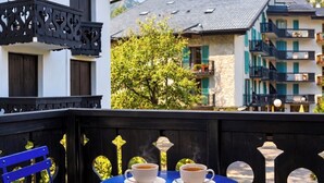 A balcony with two white cups of coffee, a blue chair, and a view of a building with balconies and a tree. - Cosy Nest Near Center Chamonix (Chamonix-Mont-Blanc)