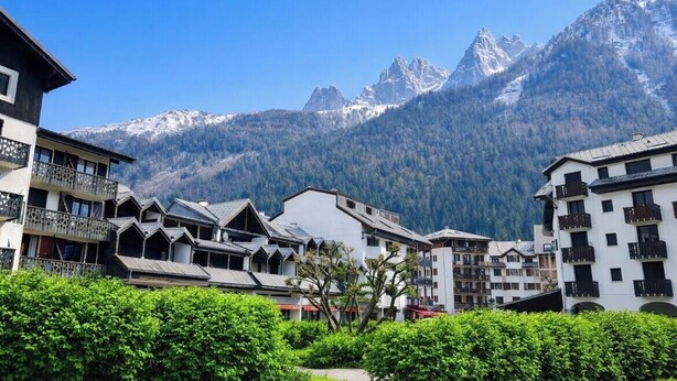 A mountain resort with chalet-style buildings, a clear sky, and snow-capped peaks in the background. - Cosy Nest Near Center Chamonix (Chamonix-Mont-Blanc)