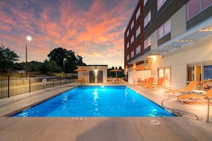 A swimming pool with lounge chairs and a building with a glass facade.