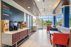 A coffee shop interior with a counter, coffee machines, seating area, and a view through the glass doors. - Holiday Inn Express and Suites Asheboro by IHG (Asheboro)