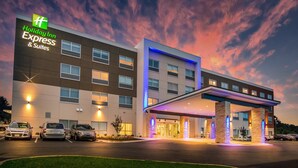 Un bâtiment de la chaîne Holiday Inn Express & Suites, doté d’un design moderne, avec une entrée couverte et un parking pouvant accueillir plusieurs voitures.