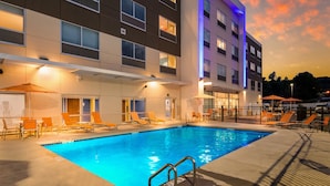 A hotel pool area with lounge chairs and umbrellas, surrounded by a modern building with multiple windows and balconies. - Holiday Inn Express and Suites Asheboro by IHG (Asheboro)