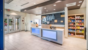 A reception area with a glass door entrance, a counter with a digital display, and shelves stocked with snacks. - Holiday Inn Express and Suites Asheboro by IHG (Asheboro)