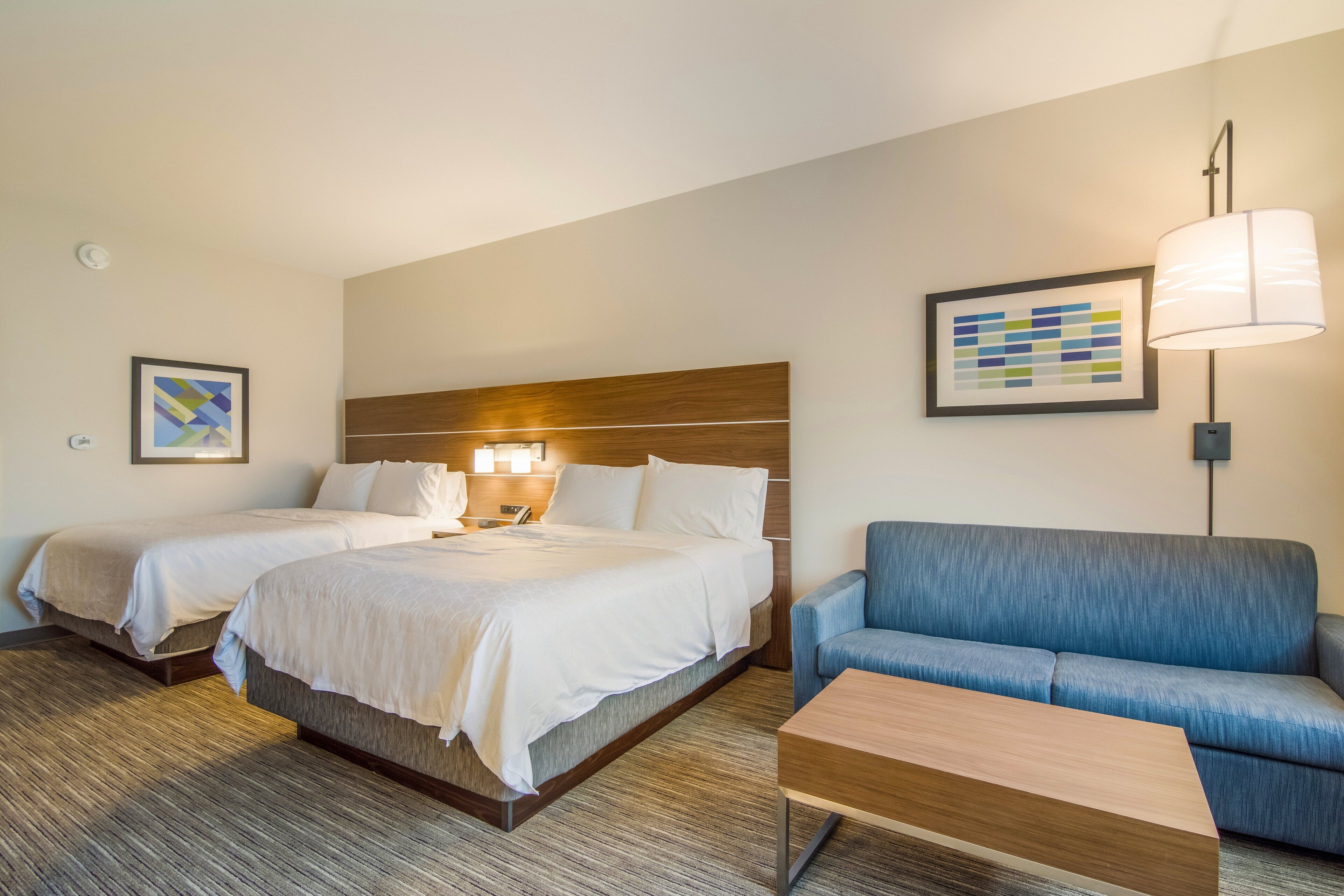 Una habitación de hotel con dos camas, un sofá azul, una mesa de centro de madera y una lámpara.