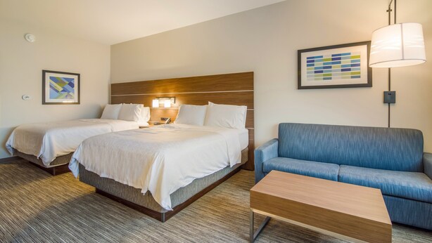 Une chambre d’hôtel avec deux lits, un canapé bleu, une table basse en bois et une lampe.
