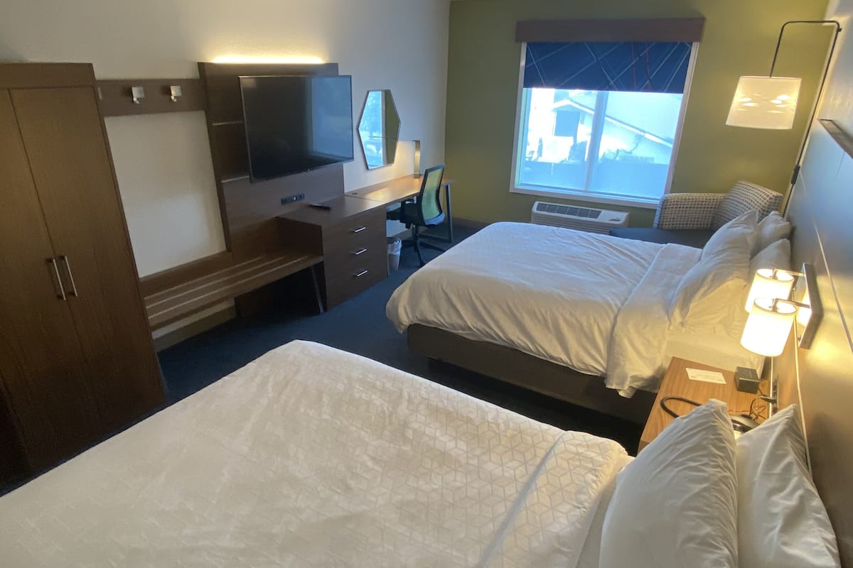 A hotel room with two beds, a desk with a computer, a TV, and a window with a view of the outside.