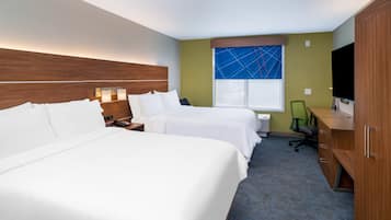 A hotel room with two beds, a desk, a chair, a TV, and a window with a blue geometric pattern.