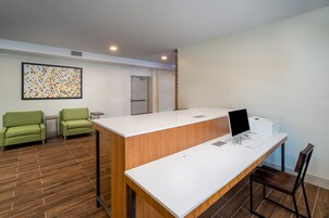Un mostrador de recepción con una computadora, una impresora y un teclado. Hay dos sillas verdes y un piso de madera.