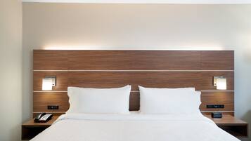 Hotellihuone, jossa on puinen sängynpääty, kaksi yöpöytää valaisimineen, valkoisilla lakanoilla varustettu sänky ja puhelin toisella yöpöydällä.