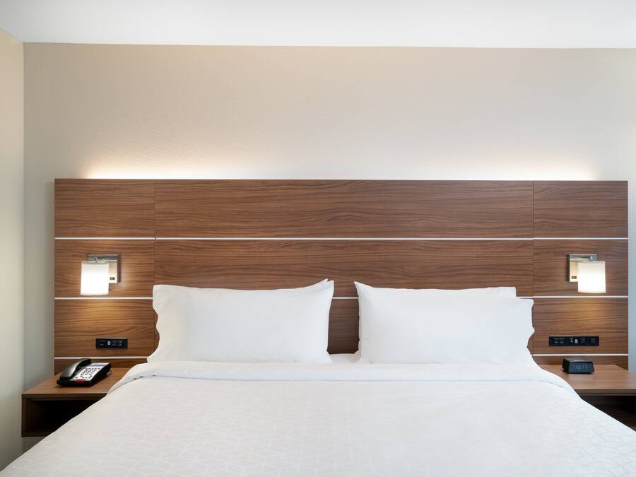Hotellihuone, jossa on puinen sängynpääty, kaksi yöpöytää valaisimineen, valkoisilla lakanoilla varustettu sänky ja puhelin toisella yöpöydällä.