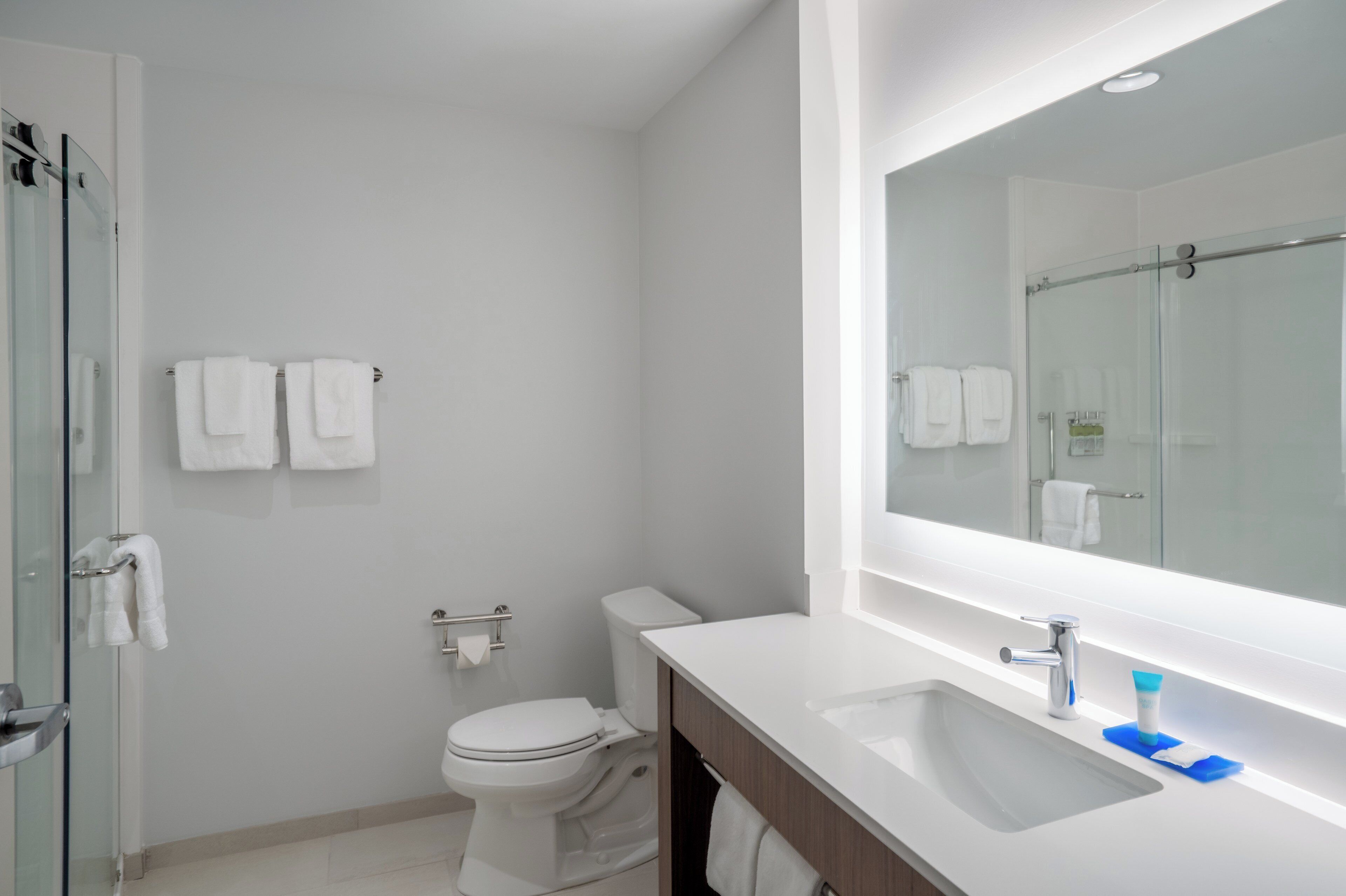 Un baño moderno con cabina de ducha de vidrio, inodoro, lavamanos con espejo y toallas blancas en la pared.