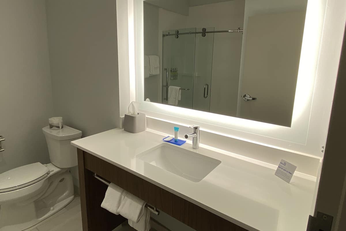 A modern bathroom with a large mirror, white sink, and a towel rack.