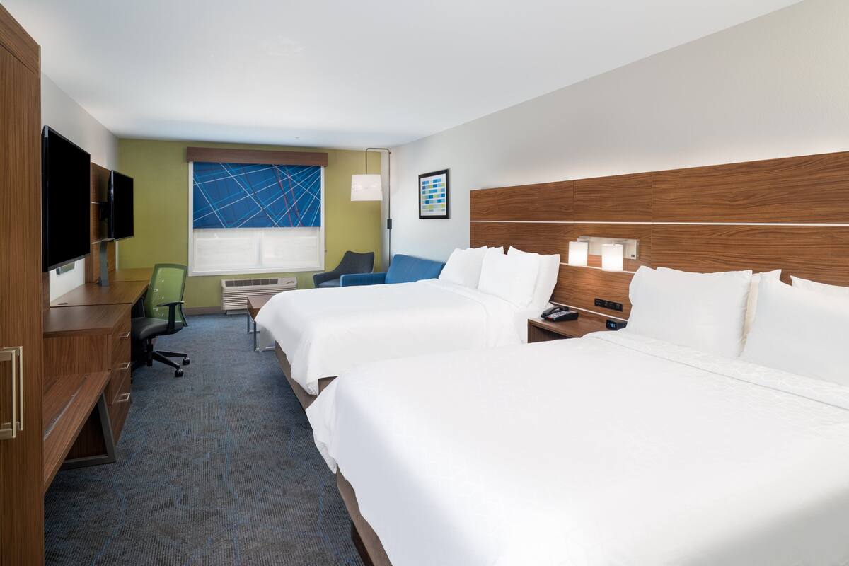 A hotel room with two beds, a desk, a chair, a TV, and a window with a blue geometric design.
