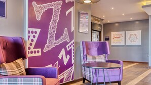 Un'elegante hall d'albergo con poltrone rivestite di viola, una parete decorata da un motivo e un tavolino rotondo.