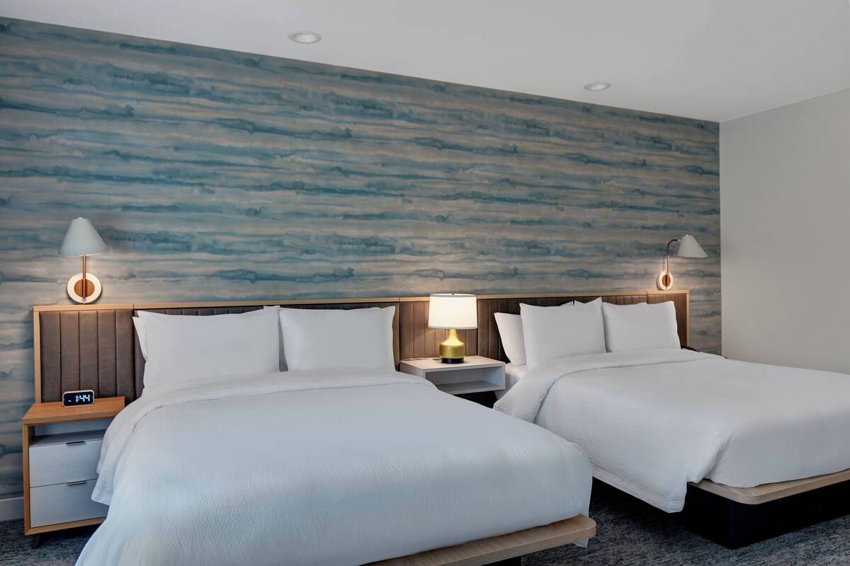 A hotel room with two beds, a wooden headboard, nightstands with lamps, and a textured blue wall.