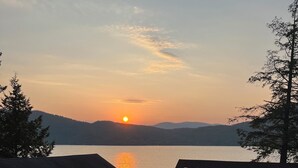A lakeside view with a sunset, cabins, and a forested area.