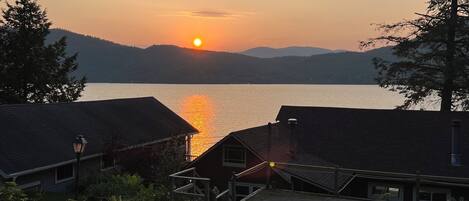 Une vue sur le lac, avec un coucher de soleil, des chalets et une zone boisée.