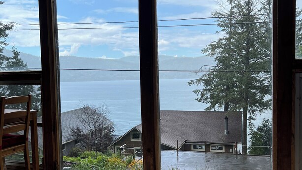 A room with large windows overlooking a body of water, a chair, and a glass table.