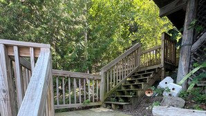 A wooden staircase leading up to a covered area, surrounded by greenery.