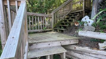 Un escalier en bois mène à une zone abritée, entourée de verdure.