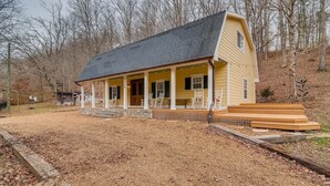 A single-story house with a porch, a stone foundation, and a yard with mulch. - Over Yonder (Leipers Fork)