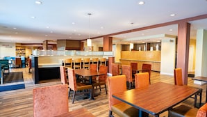 Un hall d’hôtel spacieux, doté de plusieurs espaces salon, d’un comptoir d’accueil et d’une cuisine ouverte.