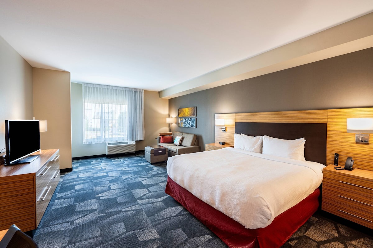 Een hotelkamer met een groot bed, een bureau, een stoel, een televisie, een lamp en een raam met gordijnen.