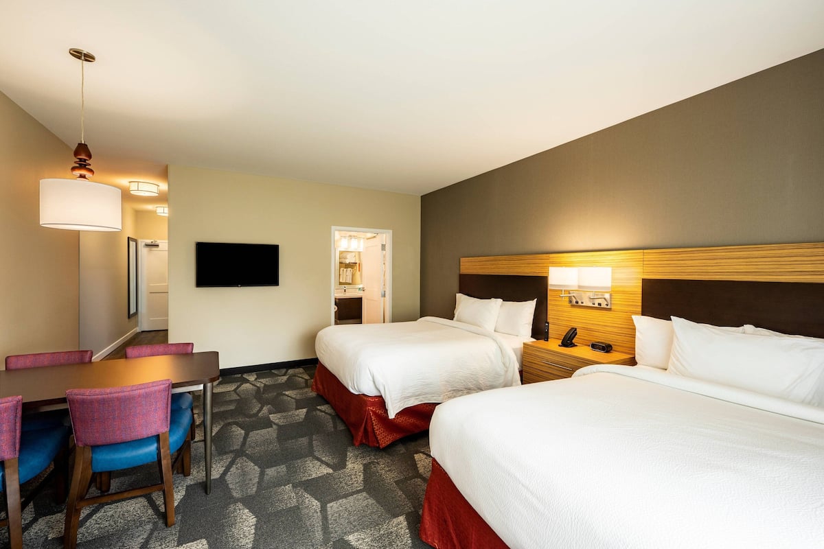 Een hotelkamer met twee bedden, een bureau met stoelen, een flatscreen televisie en een telefoon op het nachtkastje.