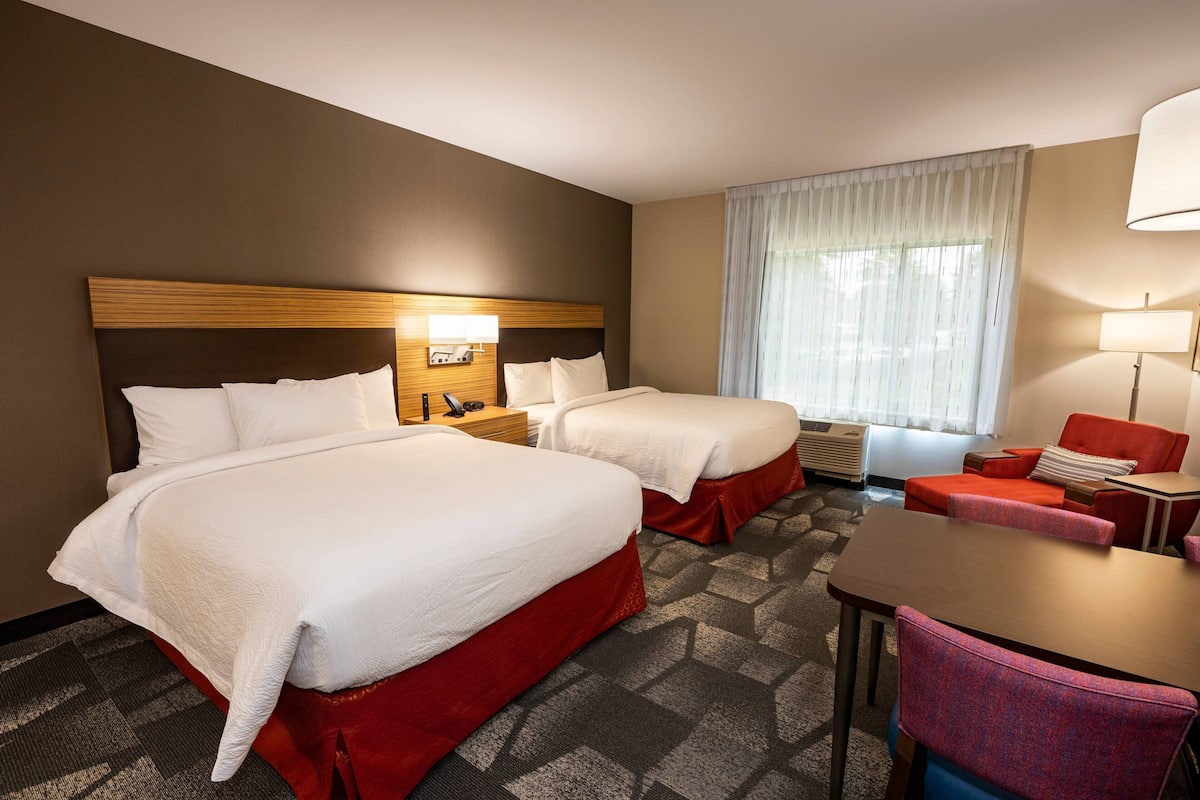 Een hotelkamer met twee bedden, een bureau, een stoel, een nachtkastje en een raam met gordijnen.