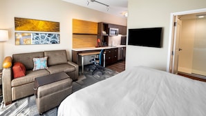 Une chambre d’hôtel équipée d’un lit, d’un canapé, d’un bureau, d’une chaise, d’une télévision et d’un four à micro-ondes.