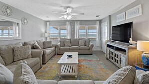 A living room with a beige sofa set, a coffee table, a TV, and a ceiling fan.