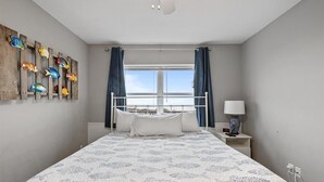 A bedroom with a bed, a nightstand, a lamp, a window with curtains, and a wall with fish art.