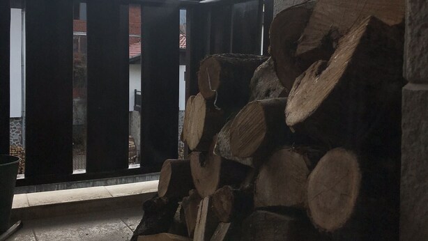 Una pila de leña frente a un edificio, con montañas en el fondo.