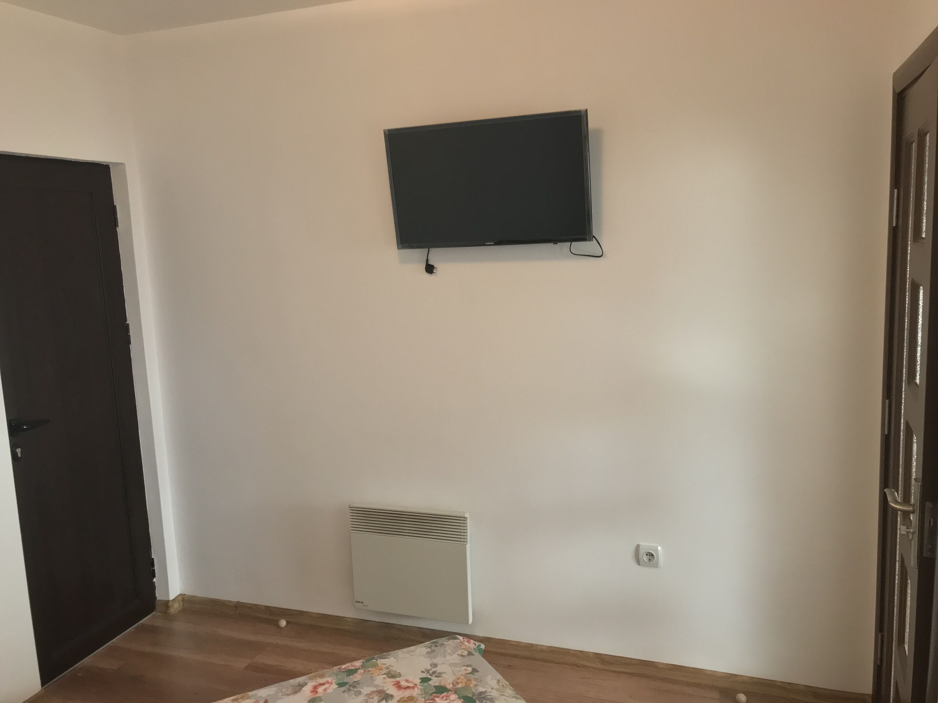 Een kamer met een aan de muur bevestigde, zwarte televisie, een witte radiator en een houten vloer.
